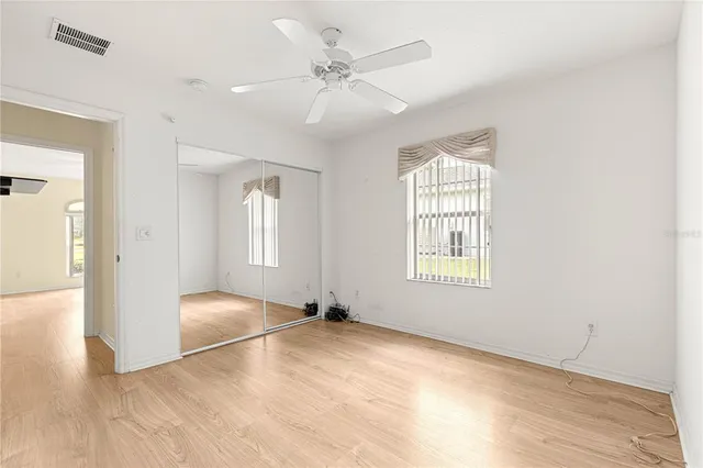 an empty room with wooden floor fan and windows