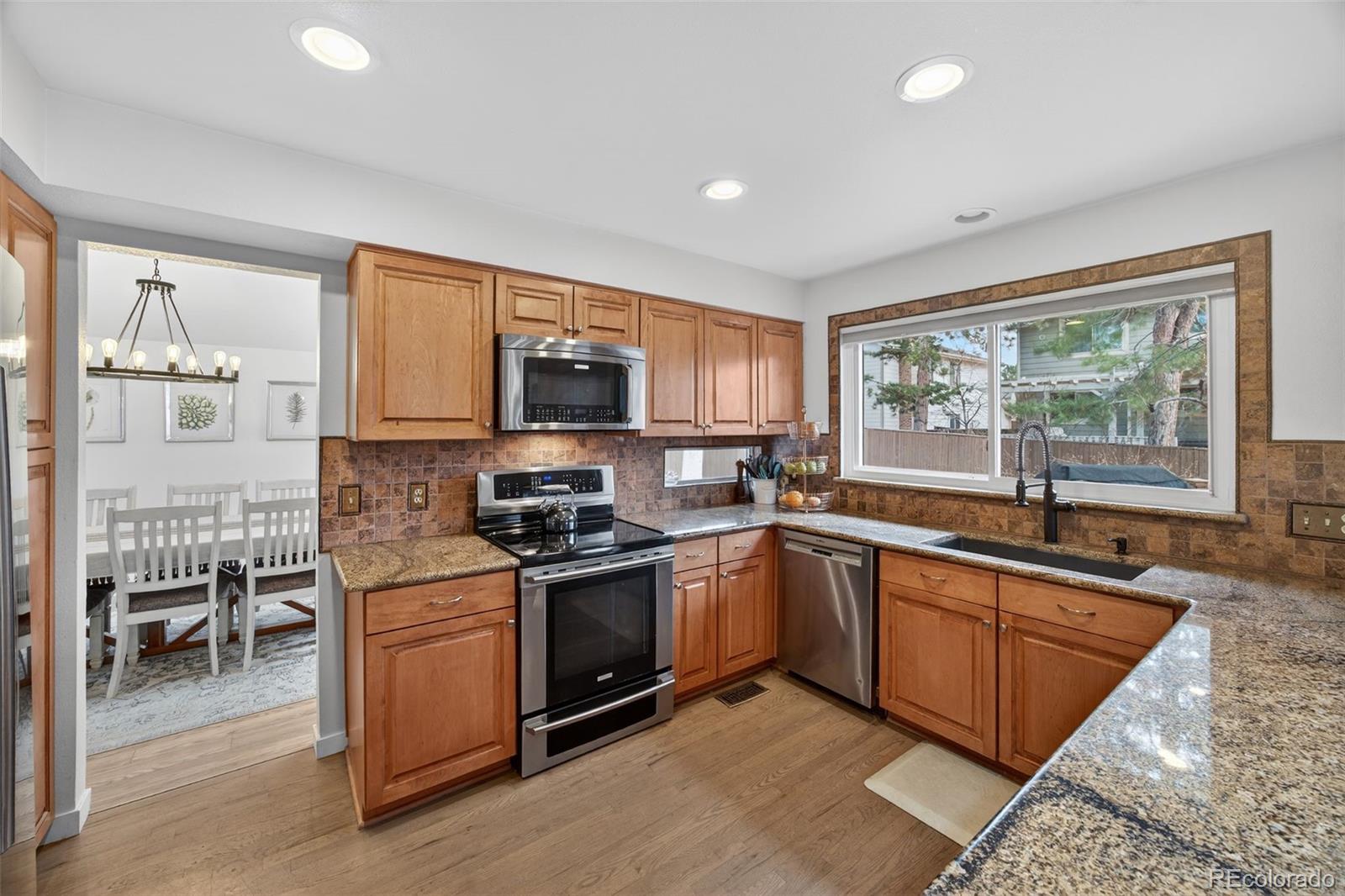 8764 Wildrose Court Highlands Ranch, CO 80126 - Photo 15 of 50 a kitchen with stainless steel appliances granite countertop a stove top oven a sink dishwasher a dining table and chairs with wooden floor