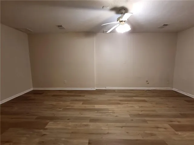 a view of an empty room with chandelier fan and wooden floor