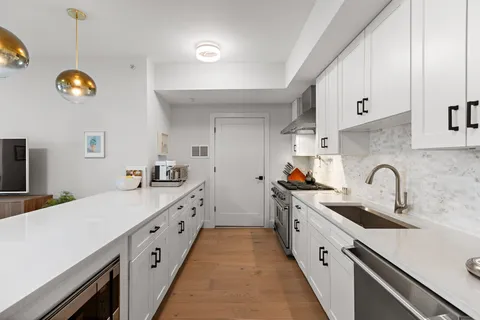 a large kitchen with stainless steel appliances a stove a sink dishwasher and white cabinets with wooden floor