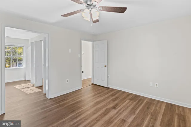 an empty room with wooden floor chandelier fan and windows