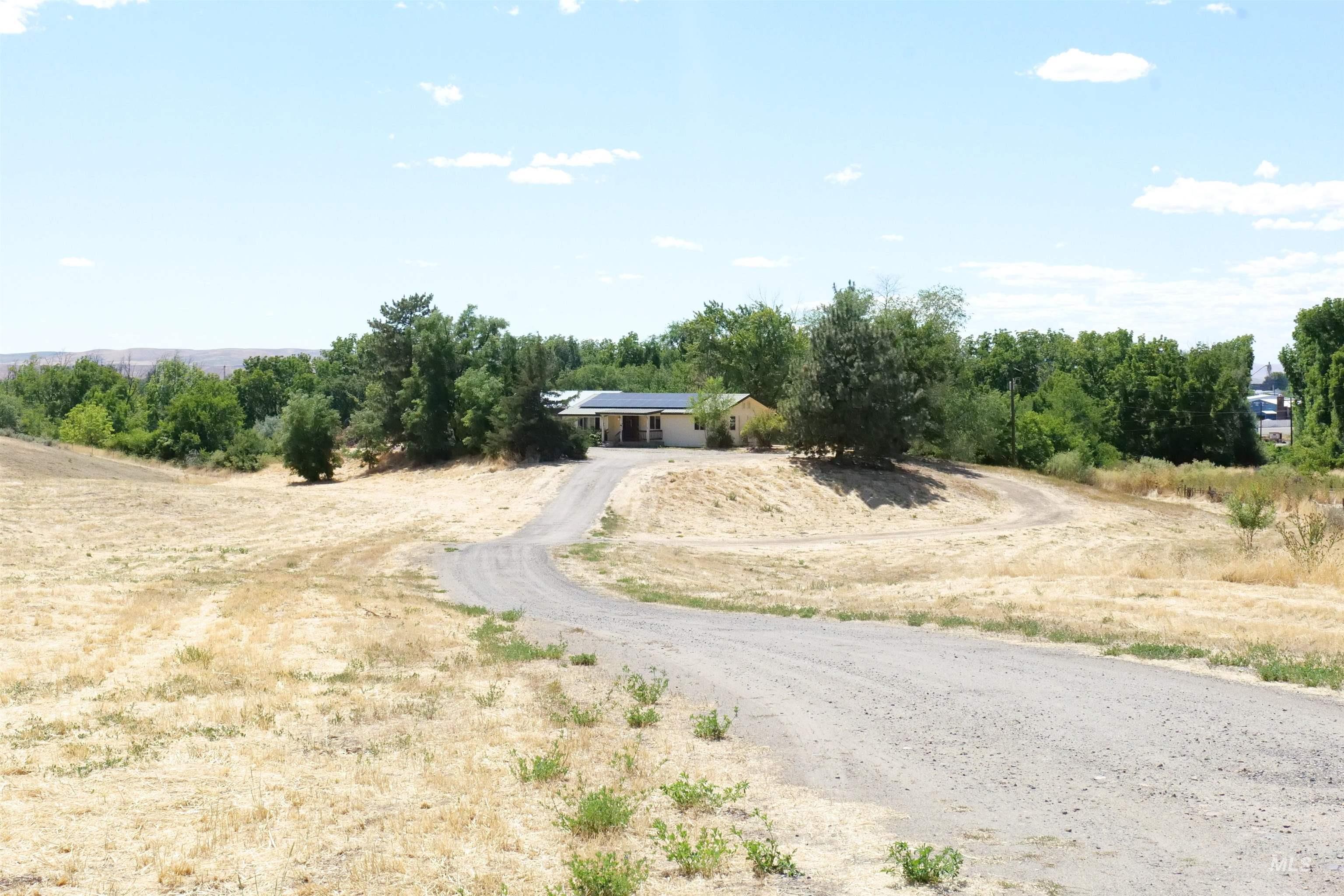 1485 East 9th Street Weiser, ID 83672 - Photo 9 of 18 Single-story residence set on a sloped landscape, featuring a gravel driveway and surrounding mature trees