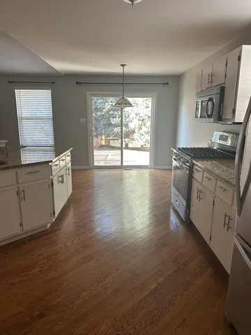 a large kitchen with stainless steel appliances granite countertop a stove a sink white cabinets and wooden floor next to a window