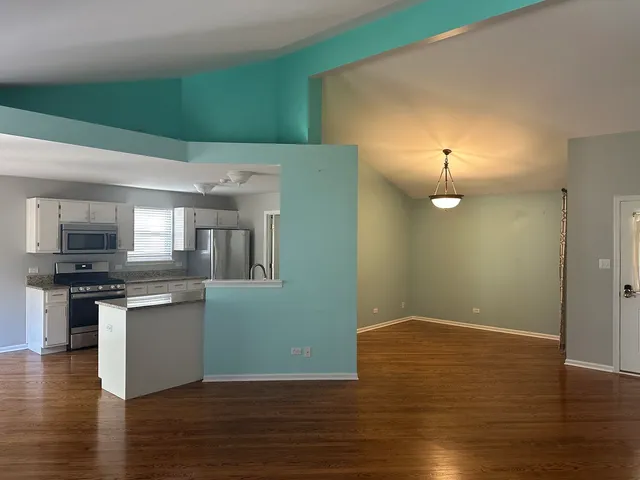 an empty room with wooden floor kitchen view and windows
