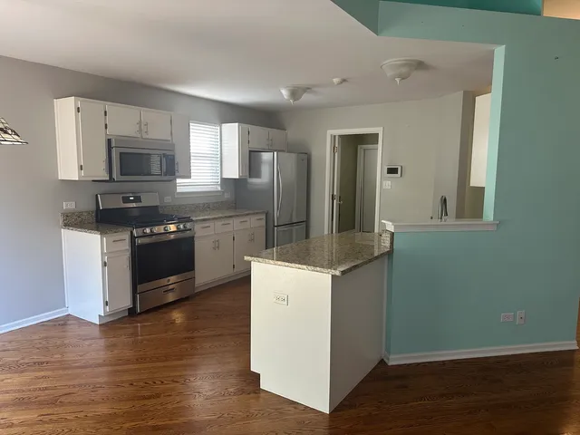 a kitchen with stainless steel appliances granite countertop a stove top oven a sink dishwasher and a microwave oven on the wooden floor