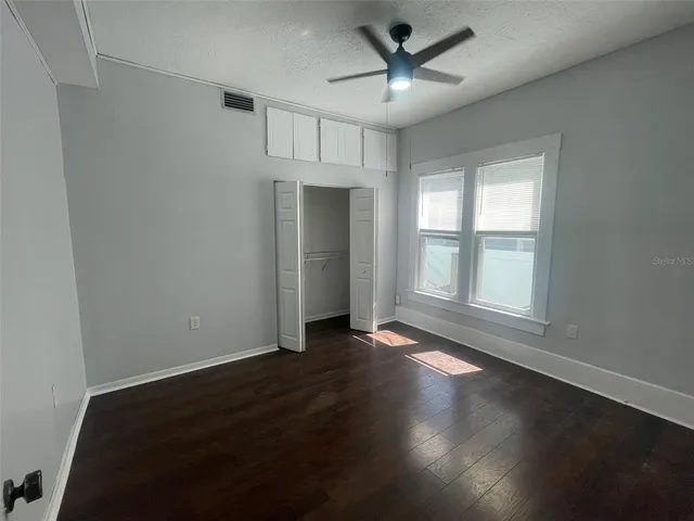 an empty room with wooden floor chandelier fan and windows