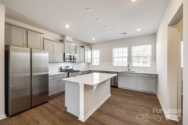 a large kitchen with stainless steel appliances granite countertop a stove a sink dishwasher a refrigerator and white cabinets with wooden floor