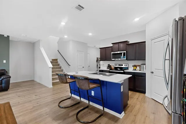 a kitchen with stainless steel appliances granite countertop a refrigerator a stove top oven a sink dishwasher and white cabinets with wooden floor