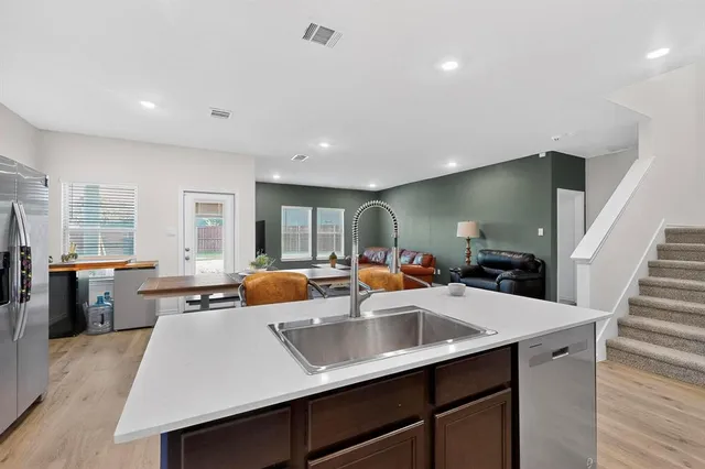 a kitchen with stainless steel appliances a sink dishwasher stove refrigerator and couches with wooden floor