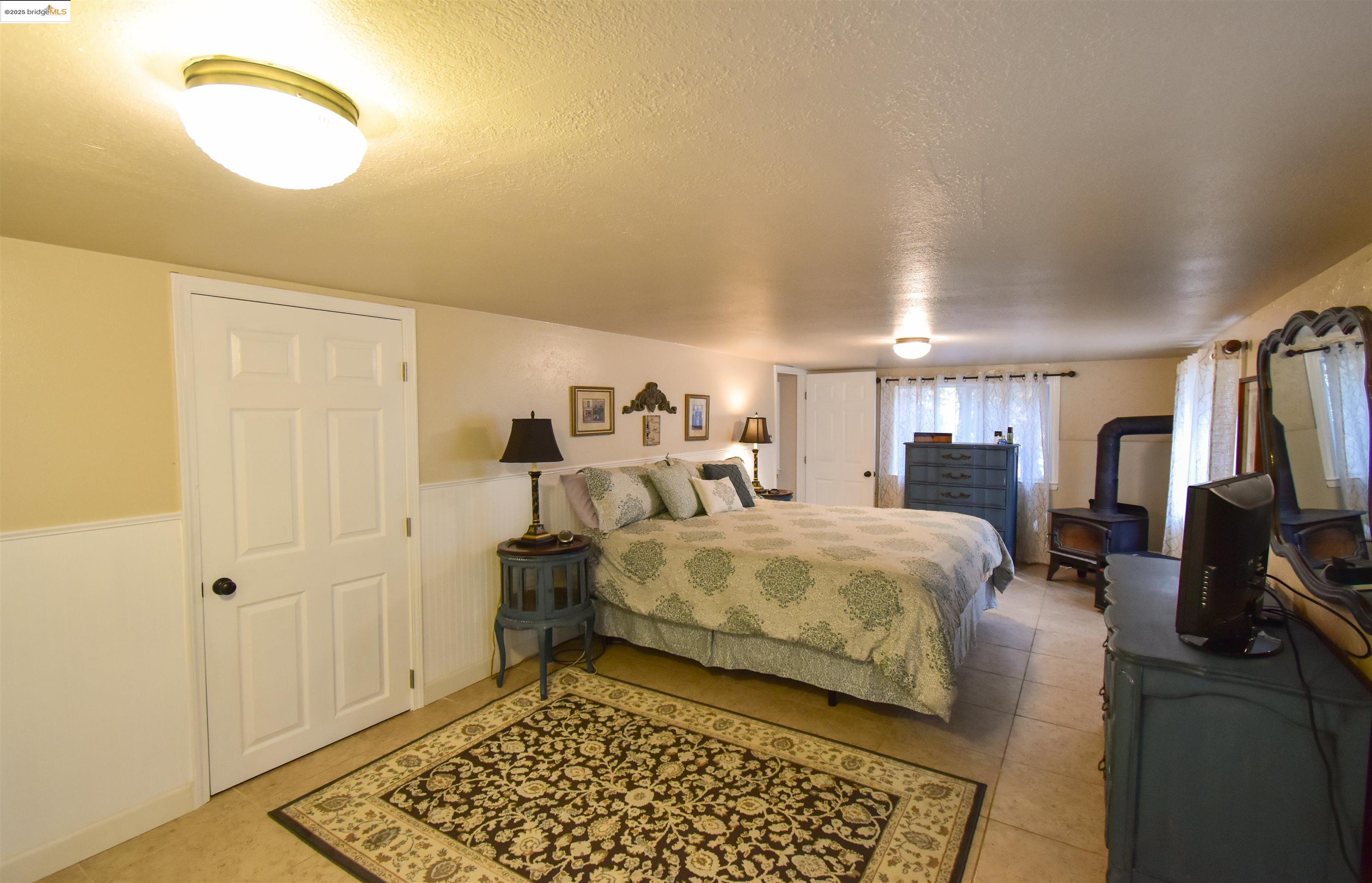 20705 Muheli Road Mi Wuk Village, CA 95346 - Photo 14 of 18 Bedroom featuring a wood stove and a wainscoted wall