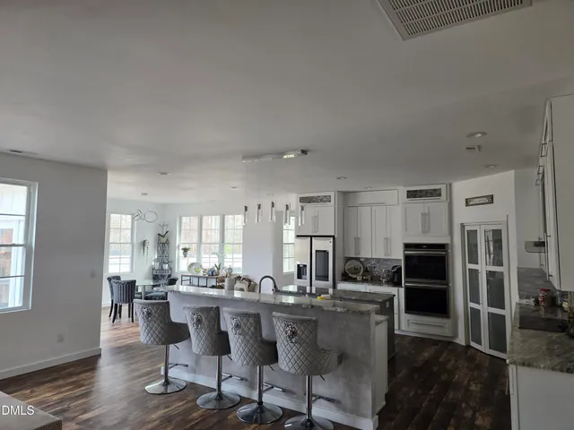 a kitchen with stainless steel appliances kitchen island granite countertop a refrigerator a stove a sink and white cabinets with wooden floor