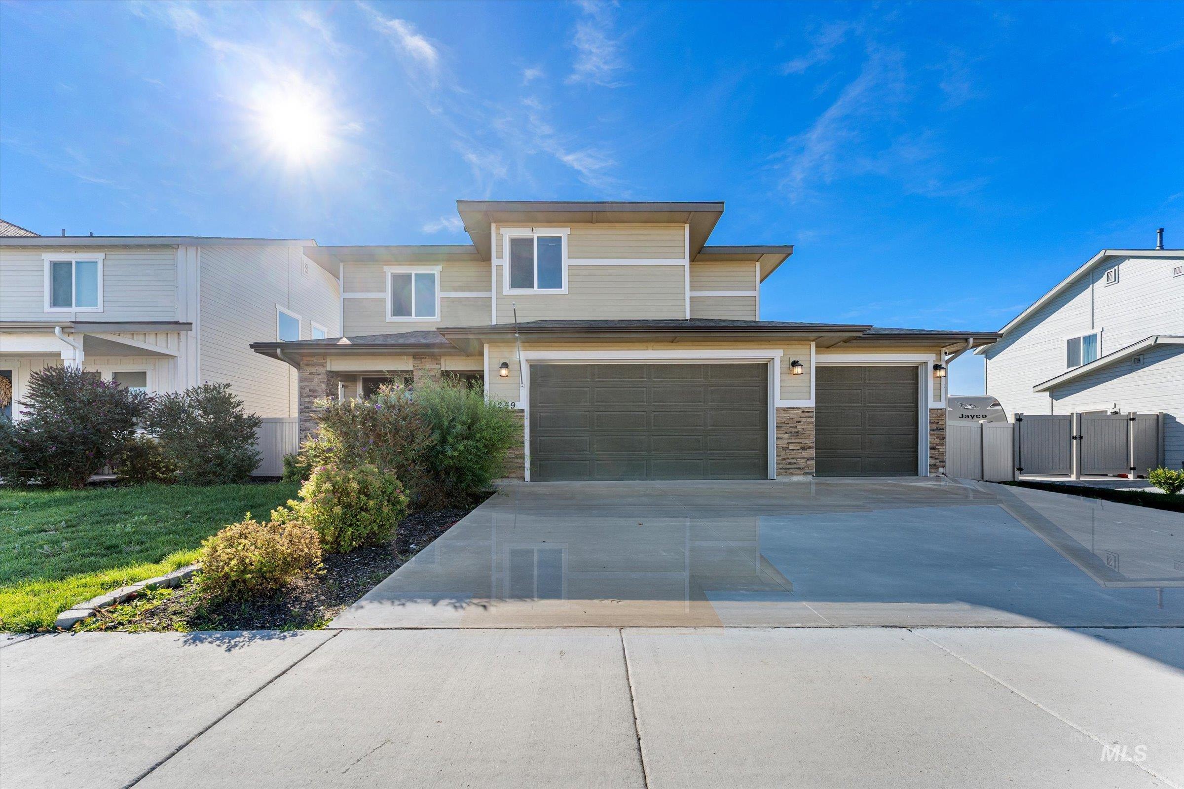View of front of property featuring concrete driveway, stone siding, a front lawn, and a gate