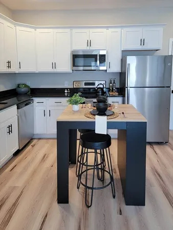 a kitchen with stainless steel appliances kitchen island granite countertop a refrigerator a stove a sink and white cabinets