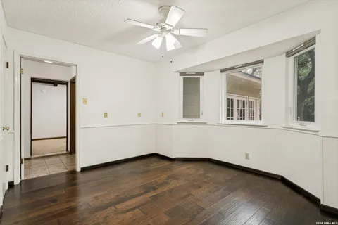 a view of an empty room with wooden floor and a ceiling fan