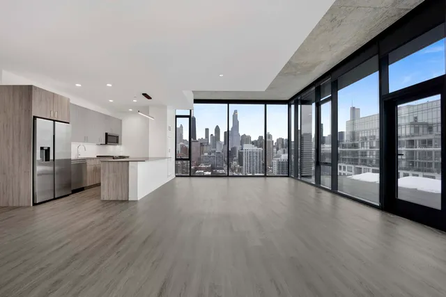 a view of an empty room with wooden floor and a kitchen