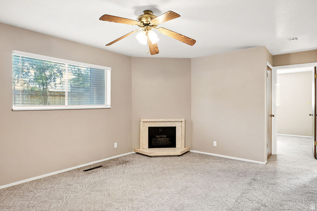 240 East 400 North, Unit 26 Logan, UT 84321 - Photo 1 of 12 Inviting room featuring a corner fireplace with a stone surround, a ceiling fan with wood-finish blades, and neutral-toned carpeting