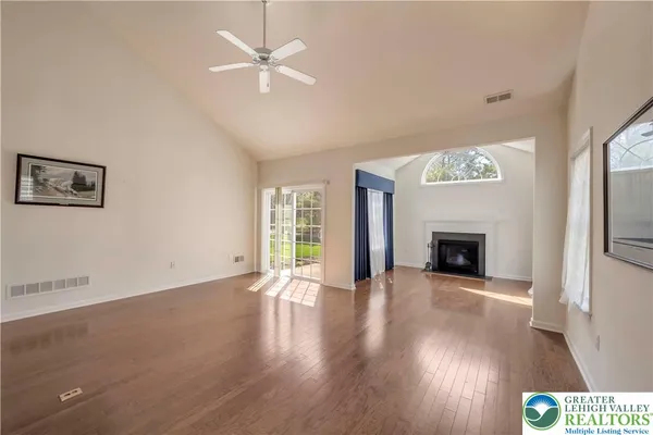 an empty room with wooden floor a ceiling fan a fireplace and windows