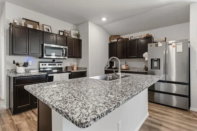 a large kitchen with granite countertop lots of counter top space a sink and stainless steel appliances