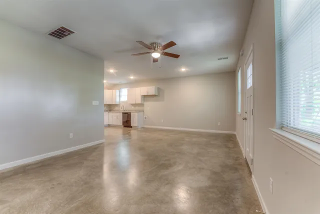 an empty room with chandelier fan and windows