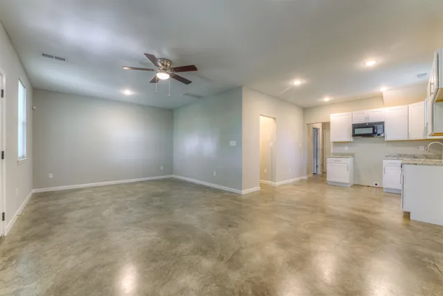 a view of an empty room with kitchen and window