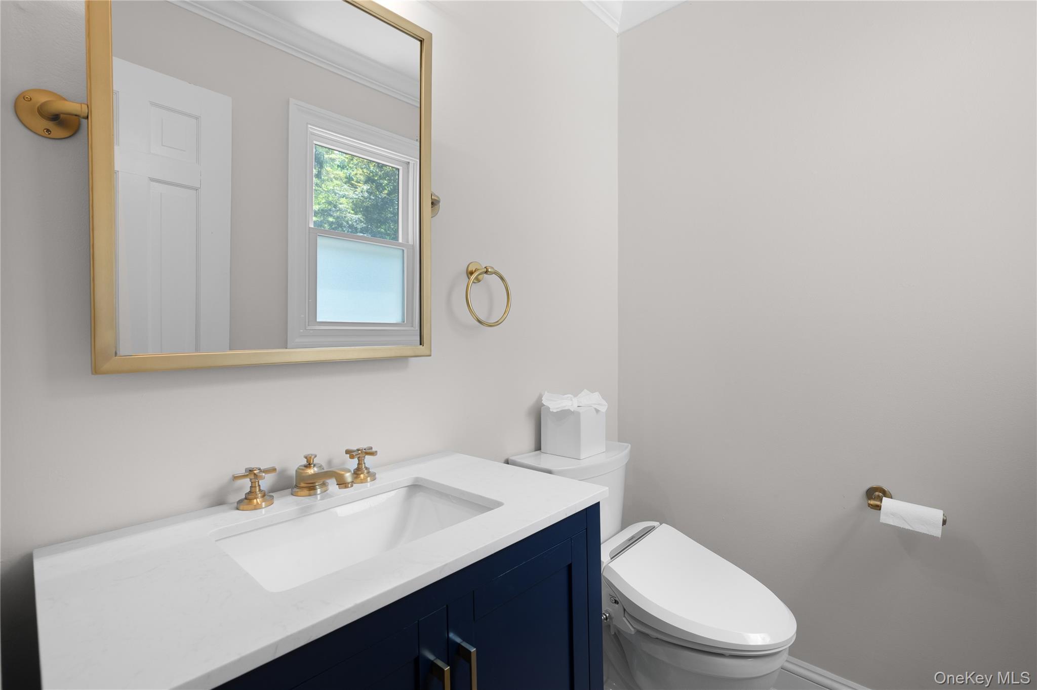 9 Three Sisters Road St. James, NY 11780 - Photo 7 of 36 Bathroom featuring a navy blue vanity with gold-finish hardware, a white integrated sink, and a gold-framed tilting mirror