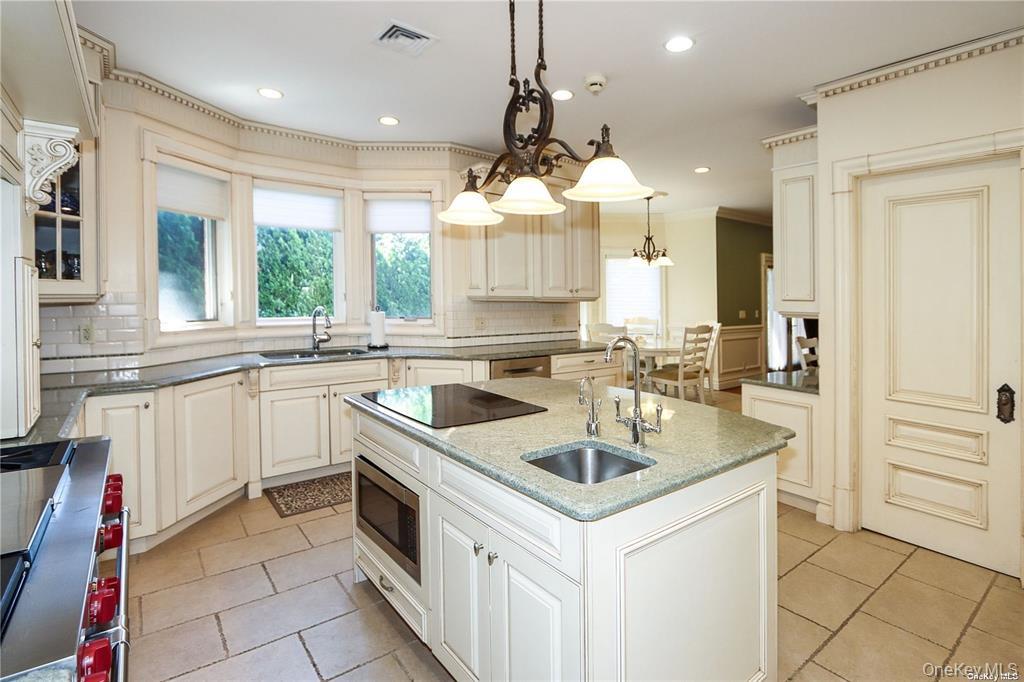 24 Steamboat Road Great Neck, NY 11024 - Photo 12 of 28 Kitchen featuring appliances with stainless steel finishes, hanging light fixtures, dark stone countertops, a kitchen island with sink, and decorative backsplash