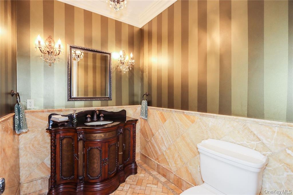 24 Steamboat Road Great Neck, NY 11024 - Photo 15 of 28 Half bathroom featuring crown molding, vanity, wainscoting, tile walls, and wallpapered walls