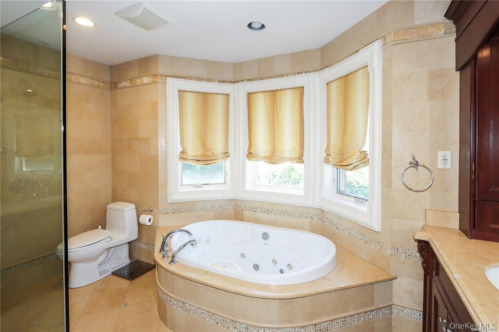24 Steamboat Road Great Neck, NY 11024 - Photo 18 of 28 Bathroom featuring tile walls, vanity, tile patterned floors, a stall shower, and a jetted tub