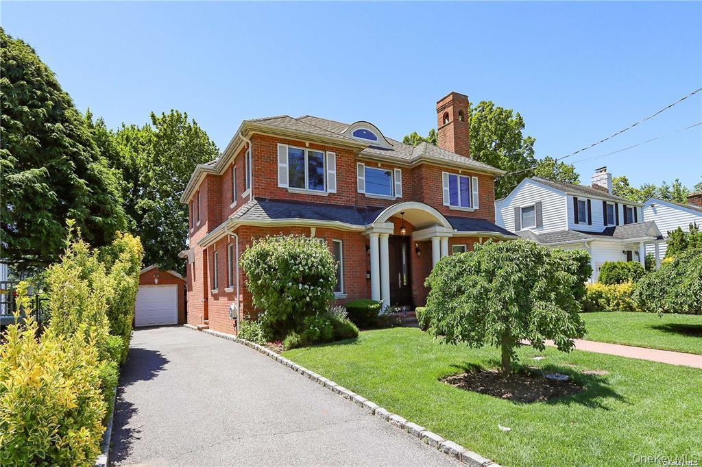 24 Steamboat Road Great Neck, NY 11024 - Photo 2 of 28 View of front facade featuring brick siding, an outdoor structure, a garage, and a front yard