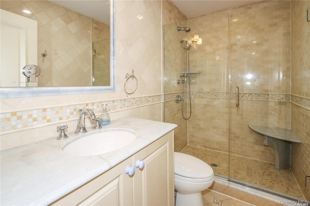24 Steamboat Road Great Neck, NY 11024 - Photo 23 of 28 Full bath with tile walls, a shower stall, vanity, light tile patterned floors, and backsplash