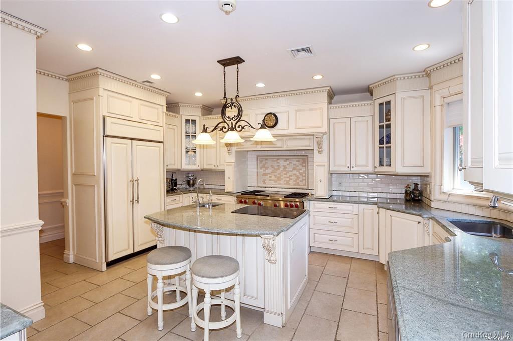 24 Steamboat Road Great Neck, NY 11024 - Photo 9 of 28 Kitchen with dark stone counters, a kitchen island with sink, hanging light fixtures, a breakfast bar, and glass insert cabinets
