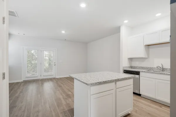 a kitchen with granite countertop a stove a sink and white cabinets with wooden floor next to windows