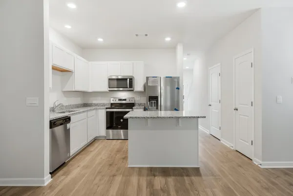 a kitchen with stainless steel appliances a refrigerator stove a sink and white cabinets with wooden floor