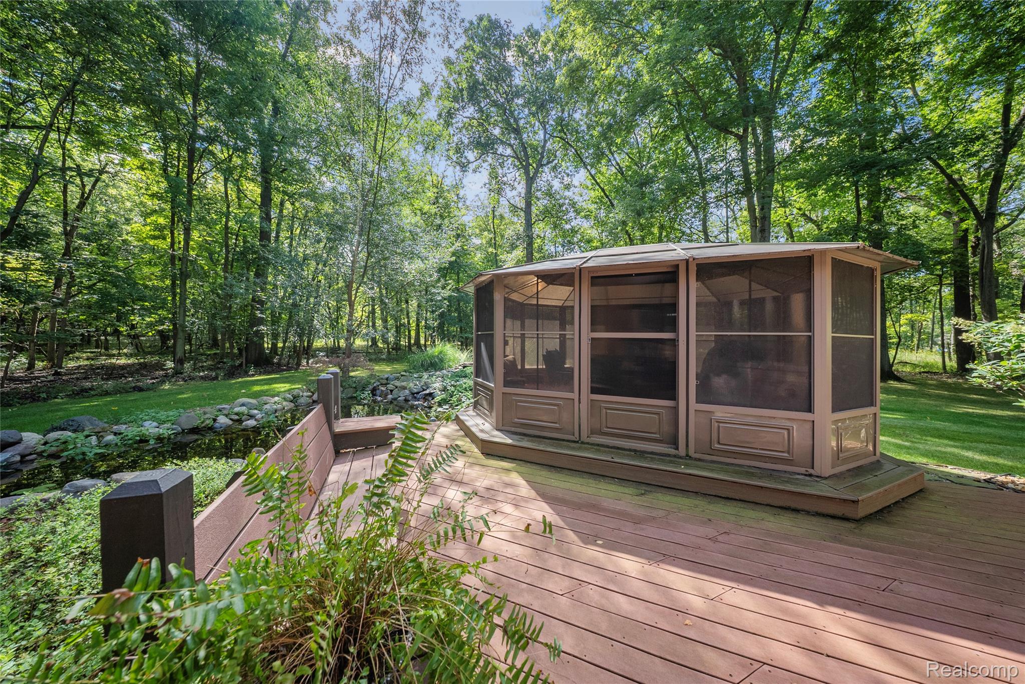 8931 Bridge Road Grosse Ile, MI 48138 - Photo 50 of 55 Expansive wood-finish deck featuring an attached screened gazebo, a built-in bench, and bordering a natural rock-lined water feature
