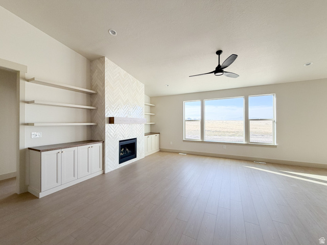 533 West S Temple Street, Unit 309 Tooele, UT 84074 - Photo 8 of 24 Unfurnished living room with a fireplace, light wood-type flooring, and a ceiling fan