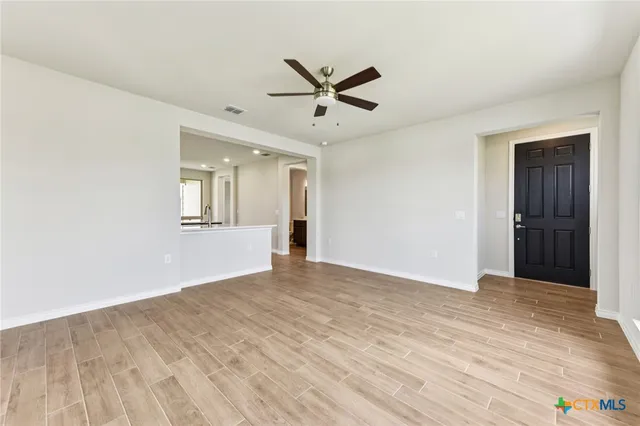 a view of an empty room with wooden floor and a ceiling fan