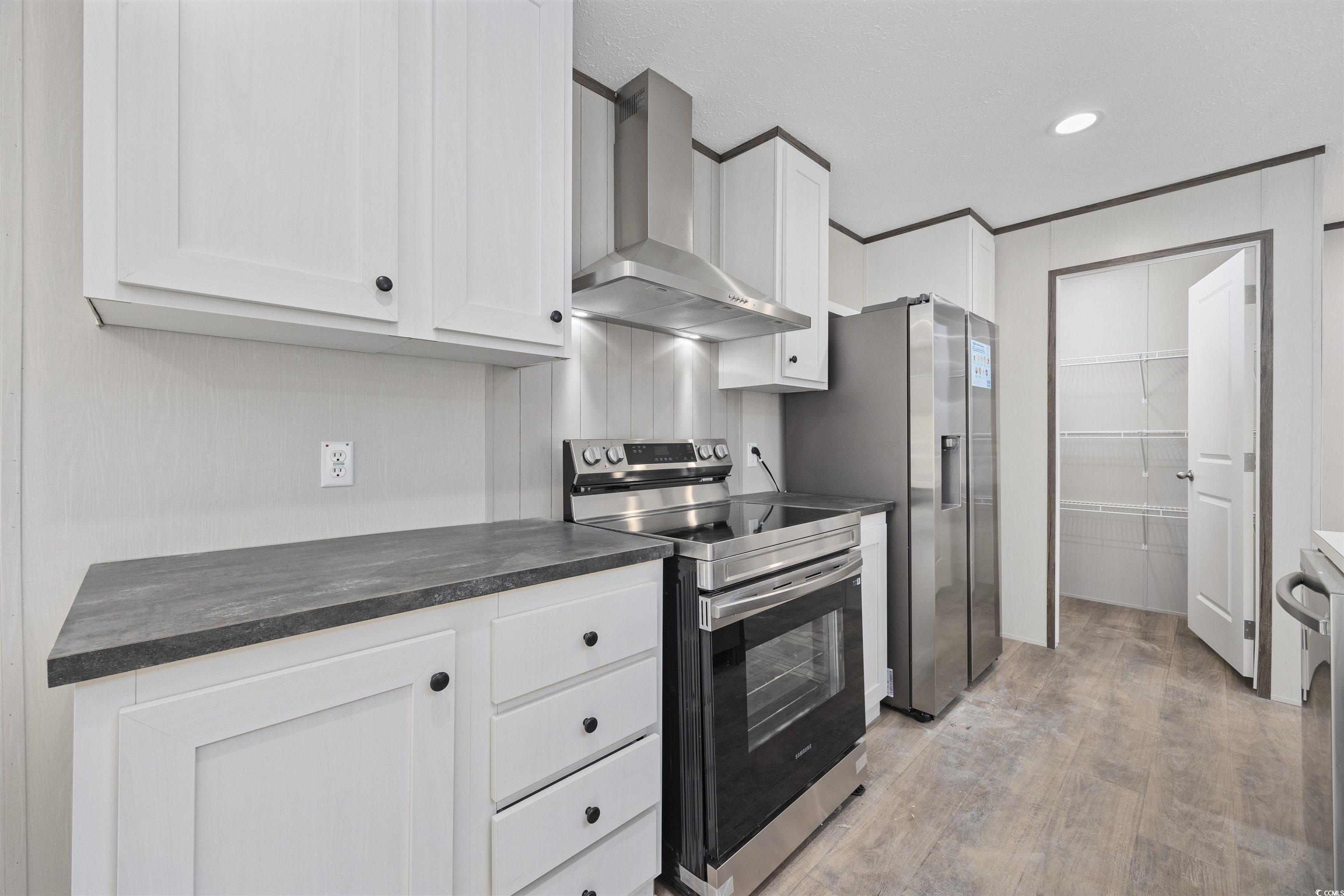 1315 Rabbit Lane Conway, SC 29526 - Photo 12 of 27 Kitchen featuring stainless steel appliances, wall chimney range hood, white cabinetry, light wood-style flooring, and ornamental molding