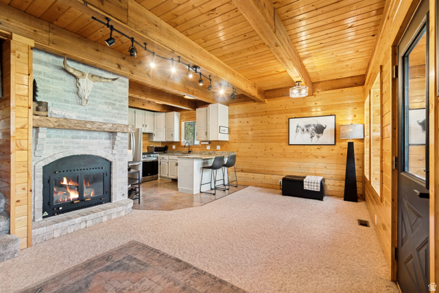 11237 East Aspen Road, Unit 74 Heber City, UT 84032 - Photo 9 of 32 Spacious living area featuring a light-colored brick fireplace with a wood mantle, wood-planked walls, and an open-concept kitchen with white cabinetry and a breakfast bar
