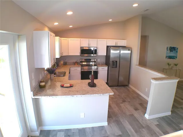 a kitchen with stainless steel appliances granite countertop a refrigerator a sink a stove and a wooden floors