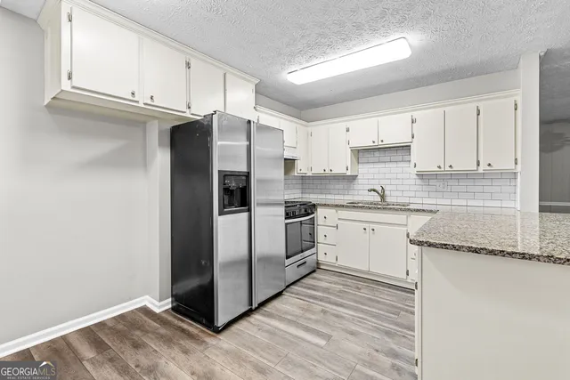 a kitchen with granite countertop a refrigerator stove and white cabinets