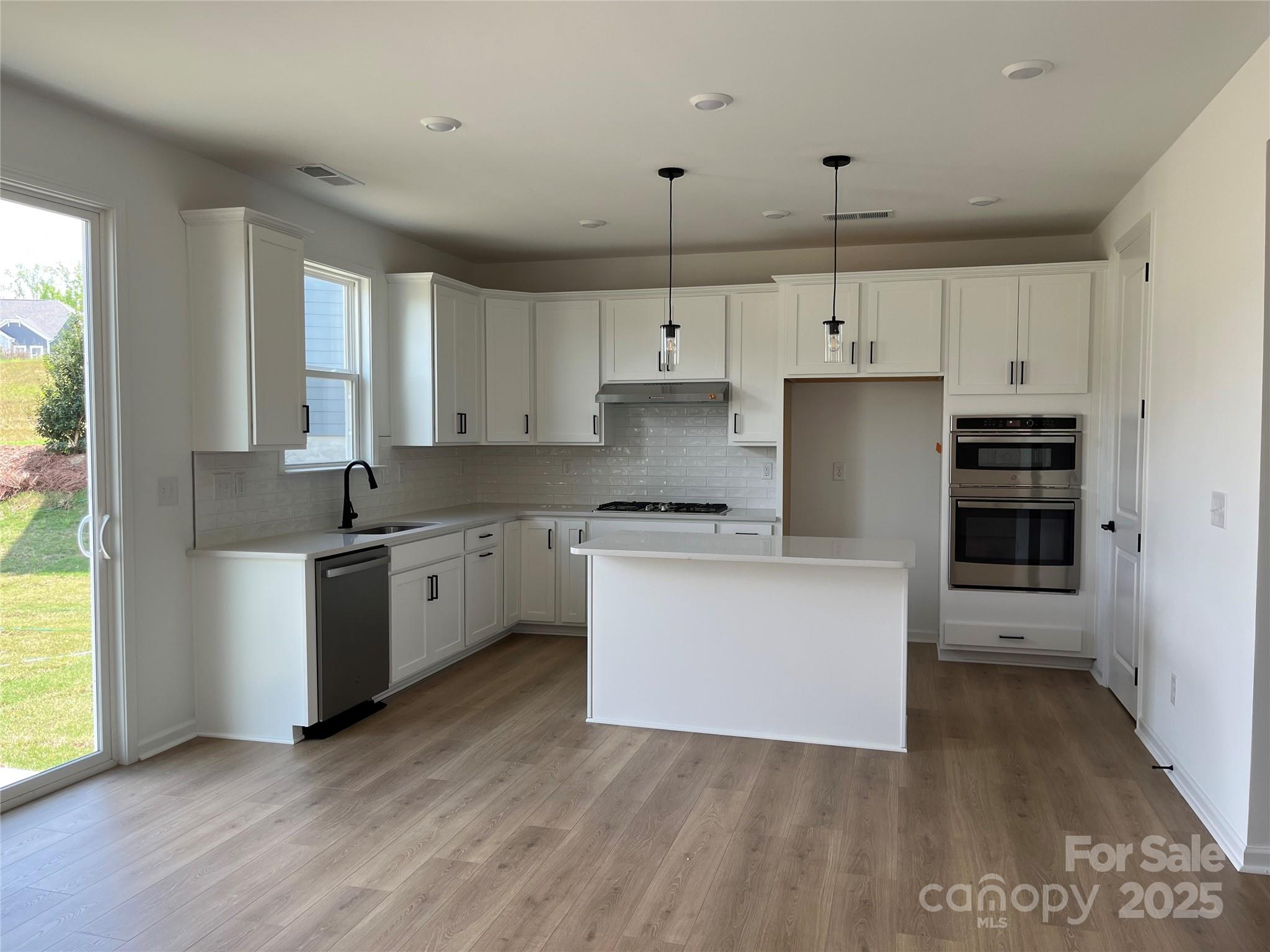 1476 Hubert Graham Way Tega Cay, SC 29708 - Photo 3 of 31 a kitchen with granite countertop a stove a sink and white cabinets with wooden floor