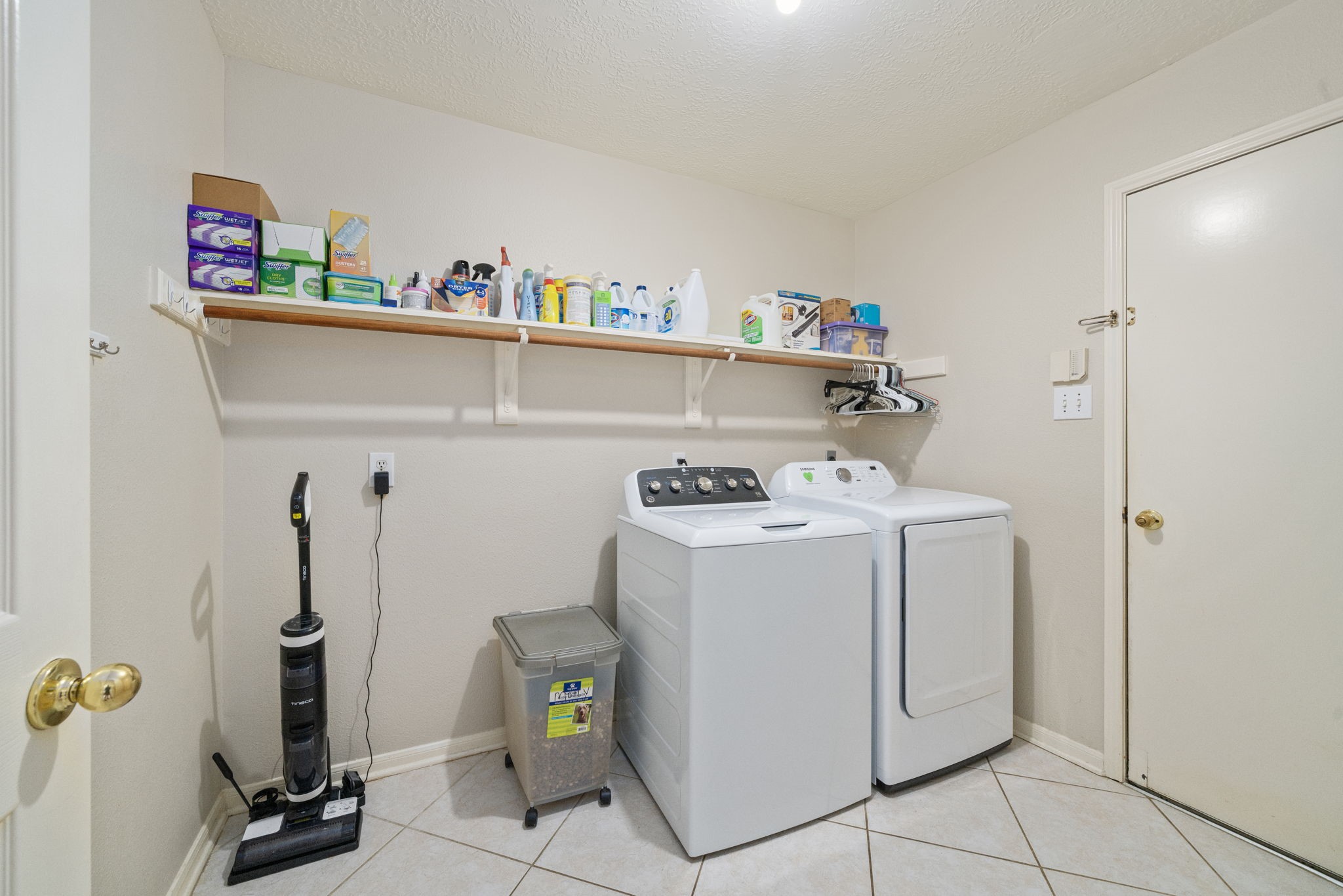 9715 Therrell Drive Houston, TX 77064 - Photo 16 of 33 Convenient full-size utility room with washer and dryer, built-in shelf and rod for storage, and tile flooring.
