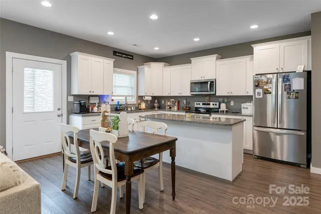 a kitchen with stainless steel appliances granite countertop a stove a refrigerator a sink a dining table and chairs with wooden floor