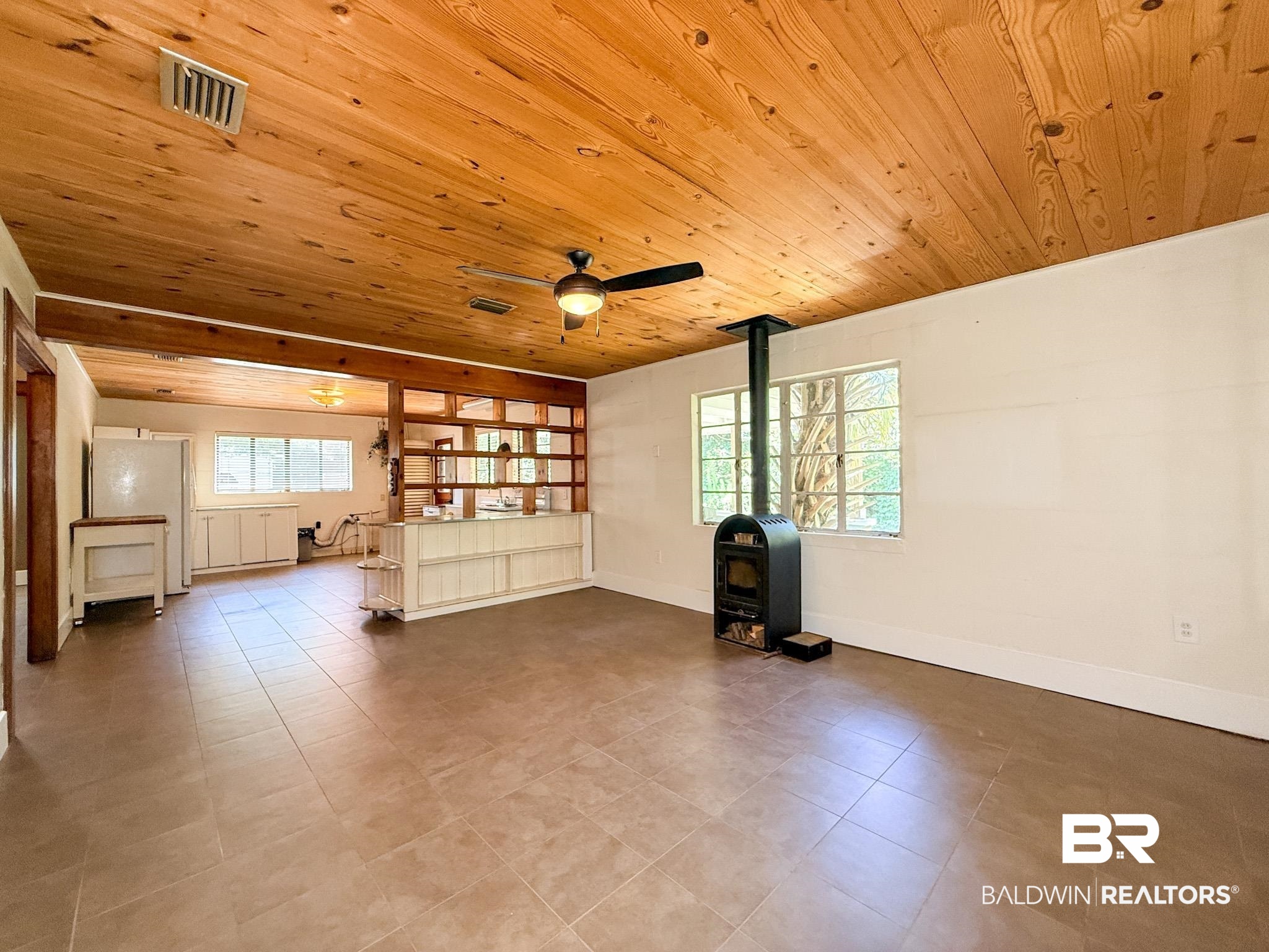 18711 Keller Road Foley, AL 36535 - Photo 5 of 38 Spacious interior featuring a wood plank ceiling, exposed wood beam, tiled flooring, built-in room divider, and a freestanding fireplace with a visible flue