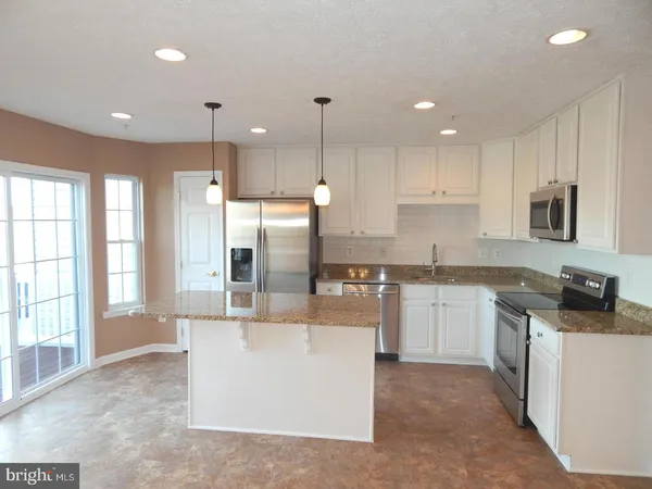 a kitchen with stainless steel appliances granite countertop a sink a stove a refrigerator and white cabinets