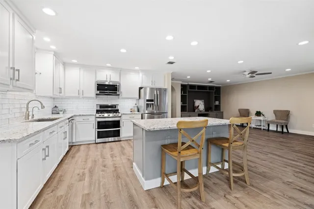 a kitchen with stainless steel appliances granite countertop a stove top oven a sink dishwasher a dining table and chairs with wooden floors