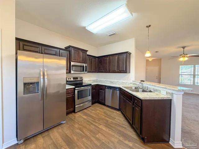 a kitchen with stainless steel appliances granite countertop a refrigerator a sink dishwasher a stove with wooden cabinets and floor