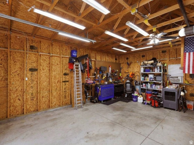 8252 Wood Street Midvale, UT 84047 - Photo 30 of 40 Spacious garage featuring exposed ceiling trusses, a ceiling fan, multiple fluorescent light fixtures, a garage door opener system, and durable concrete flooring