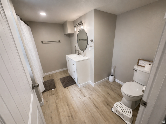 303 North Main Street Grace, ID 83241 - Photo 19 of 22 Bathroom featuring light wood-finish flooring, a white vanity with integrated sink, an oval mirror, and a toilet
