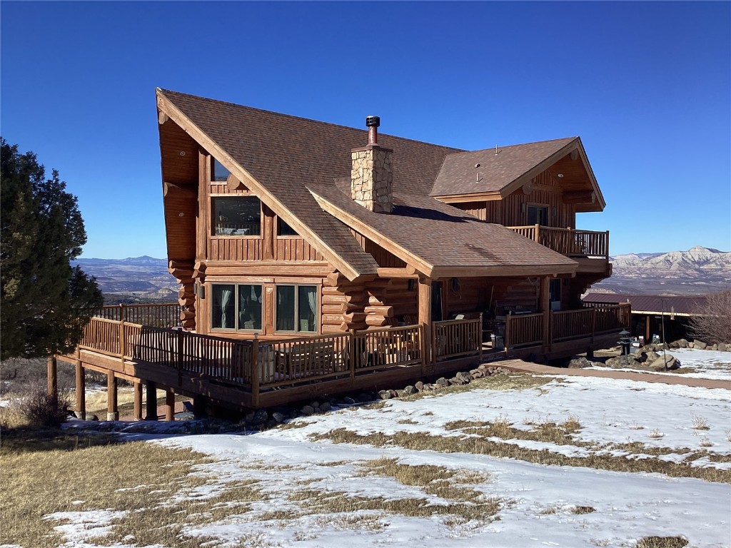 9073 54 7/10 Road Molina, CO 81646 - Photo 3 of 38 Snow covered property featuring log exterior, a shingled roof, a chimney, a balcony, and a deck with mountain view